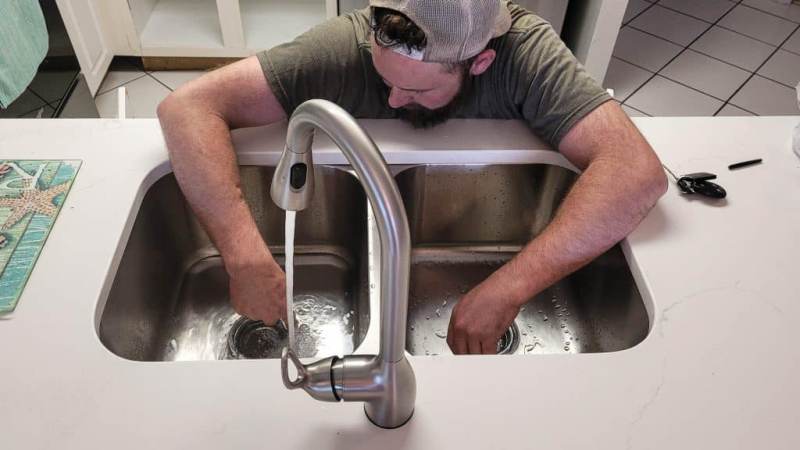 homme qui a les mains dans l'évier pour déboucher la canalisation